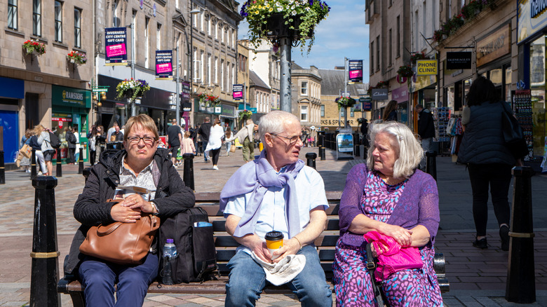 Three people chatting on a bench in Inverness, Scotland.