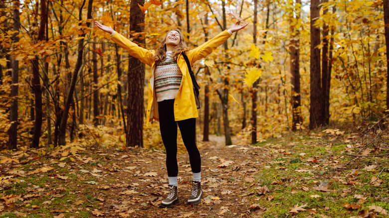 A smiling woman looking at the sky on a hiking trail with yellow leaves all around