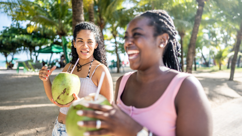 Two laughing travelers sipping on coconuts