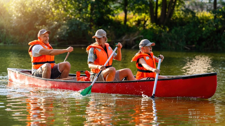 Two adults and a child paddle a canoe over glistening water