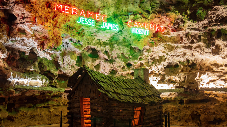 Meramec Caverns neon sign on a cave wall above a log cabin.