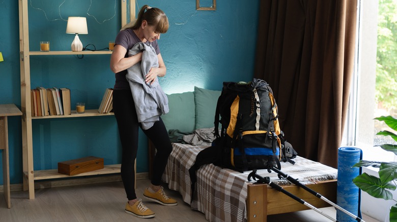 A hiker prepares to pack her sweatshirt into a backpack in her bedroom