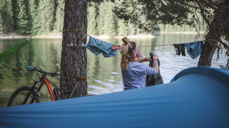 A woman hangs laundry at a riverside campsite