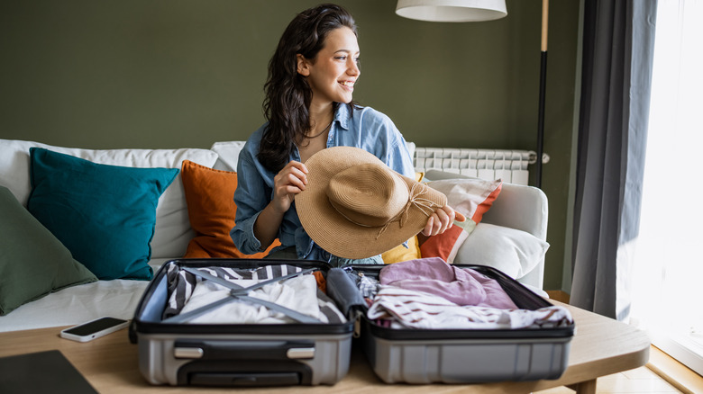 Woman holding hat over open suitcase