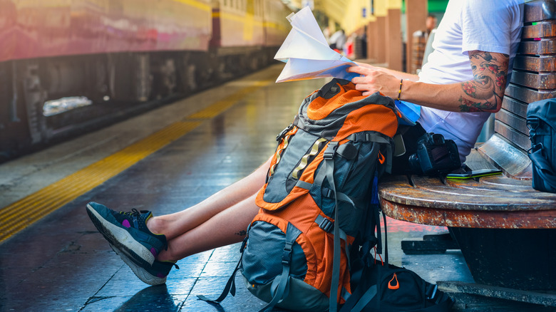 A travelers waits for a train with a map and backpack