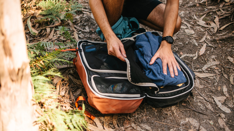 A hiker reorganizes and front-loading backpack on the ground