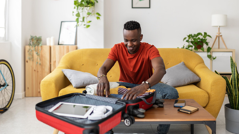 young man packing suitcase smiling