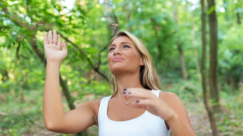 A woman swats pesky bugs in the woods