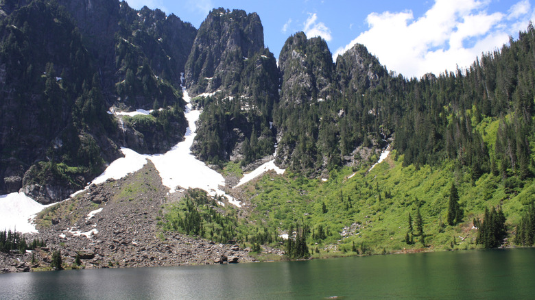 steep mountain cliffs with evergreens and grass, lake