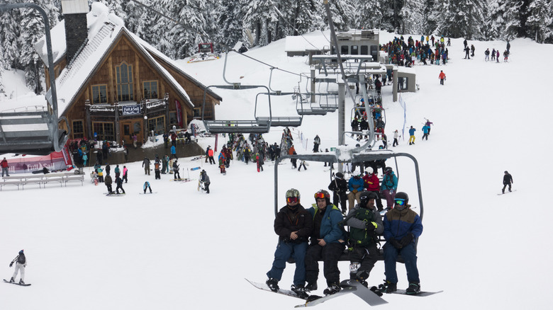 snowboarders on a ski lift, lodge and other skiers in the background