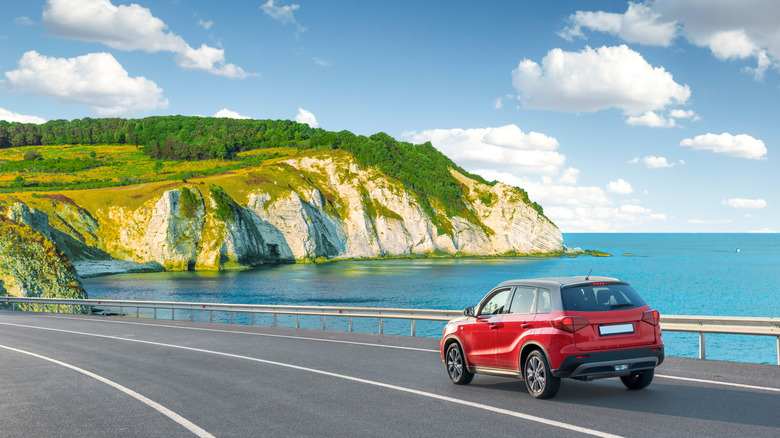 red car driving by cliffs on sunny day