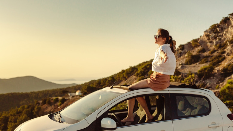 woman sitting on top of car at sunset