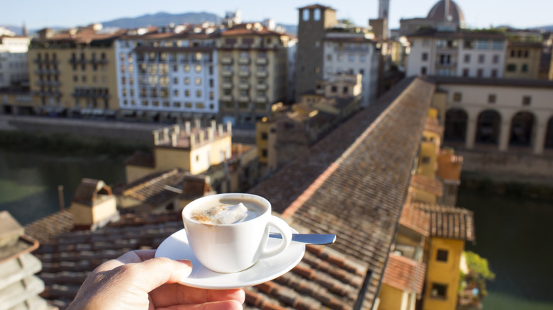 A cup of coffee is held in front of an urban Italian skyline