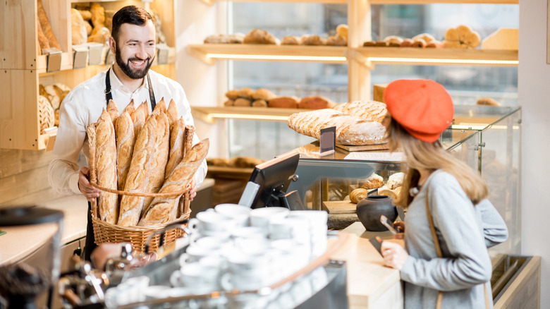 woman at checkout counter talking to a baker with baguettes
