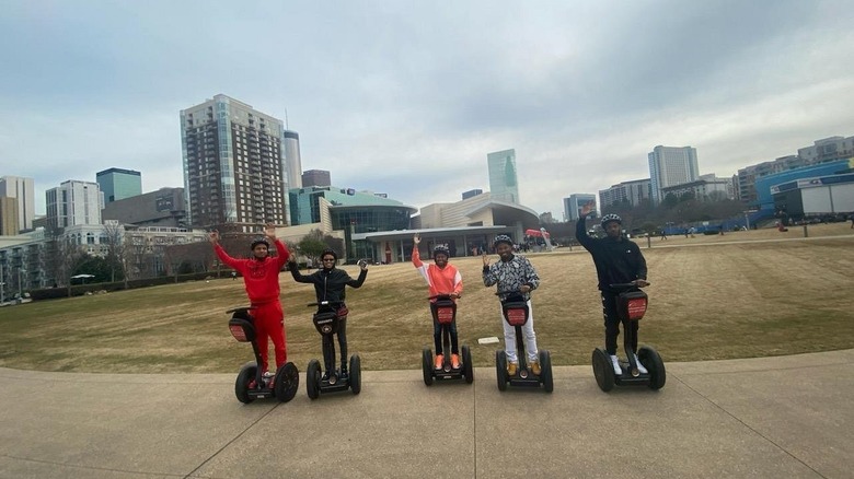 A group of people posing and waving on Segways in front of city buildings.
