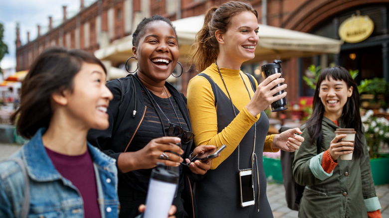 Happy multi-ethnic female friends with drinks walking on street