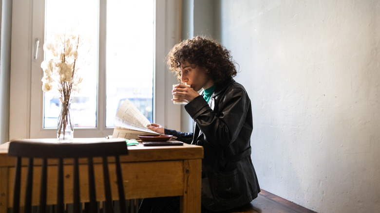 A woman reads a newspaper at a table