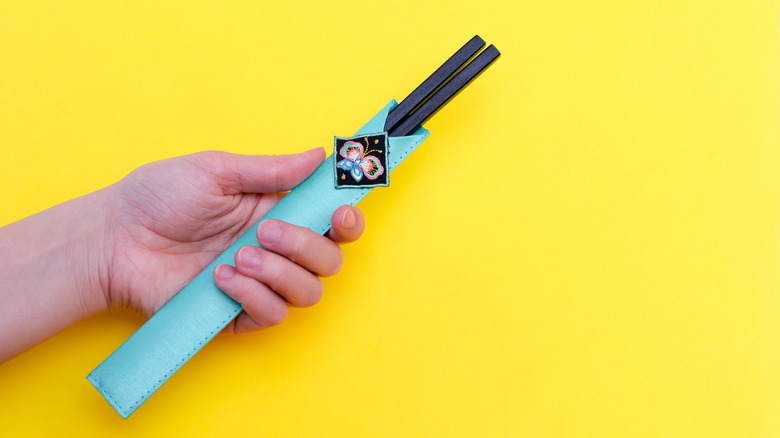 A hand holds chopsticks inside a cloth pouch