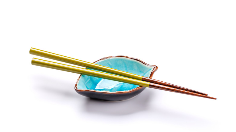 Two shiny chopsticks rest on a ceramic shell