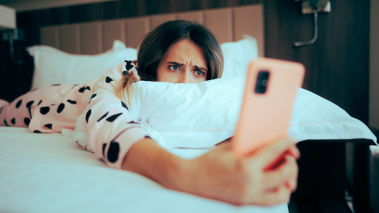 A woman in bed frowning at her phone.