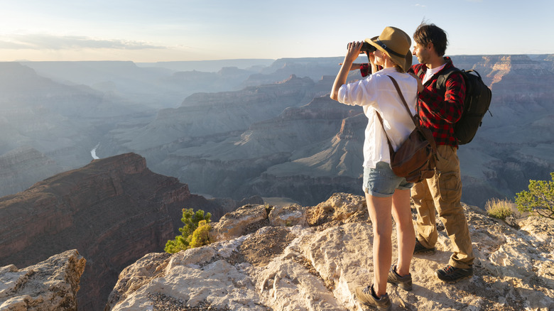 A man and woman with binoculars watching nature from a mountaintop.