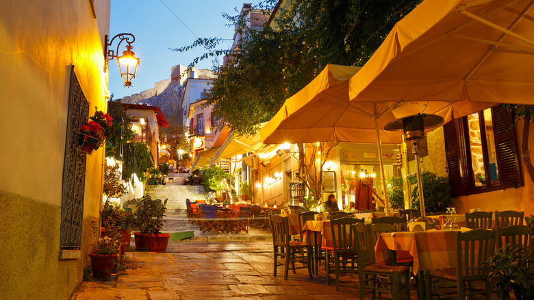 A stone path with restaurant seating and the Acropolis visible at the end of the street
