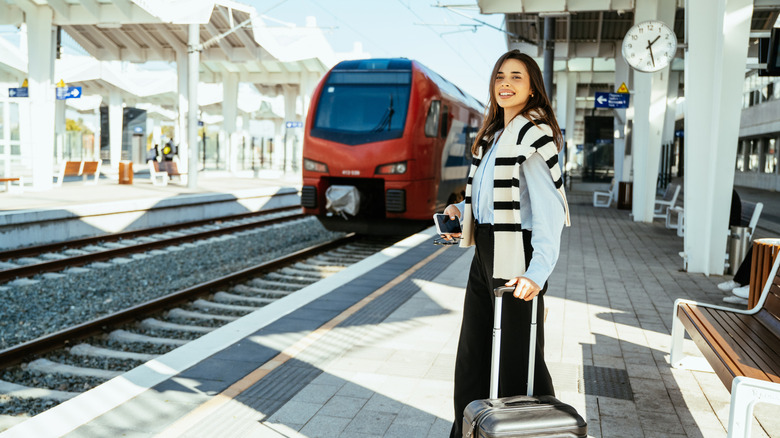 A young woman with a suitcase standing on a railway station platform.