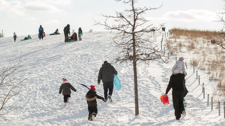 adults and children carrying sleds up a snowy hill