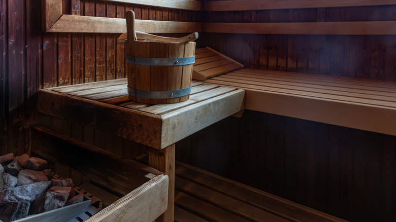 Wooden seat and bucket in sauna room with stone heater