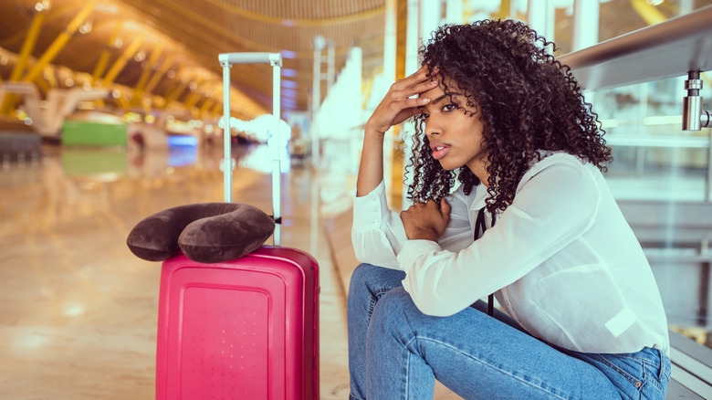 Young woman at airport with head in hand