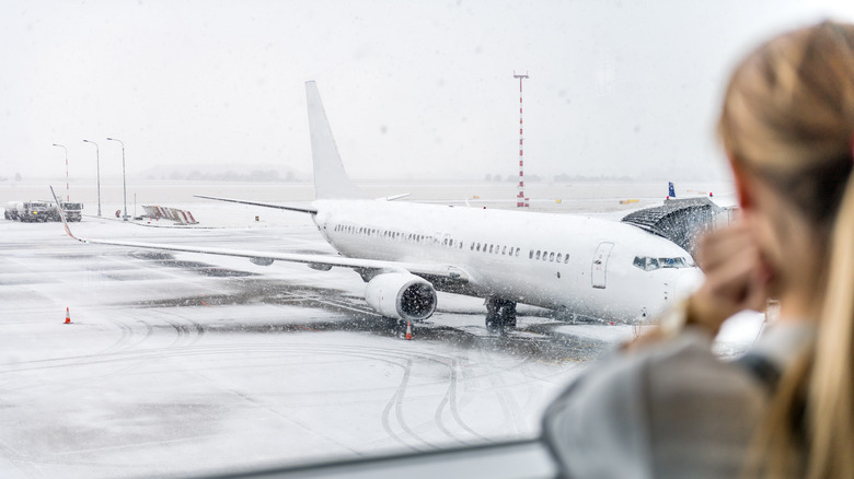 A woman looking out a window at plane in snow