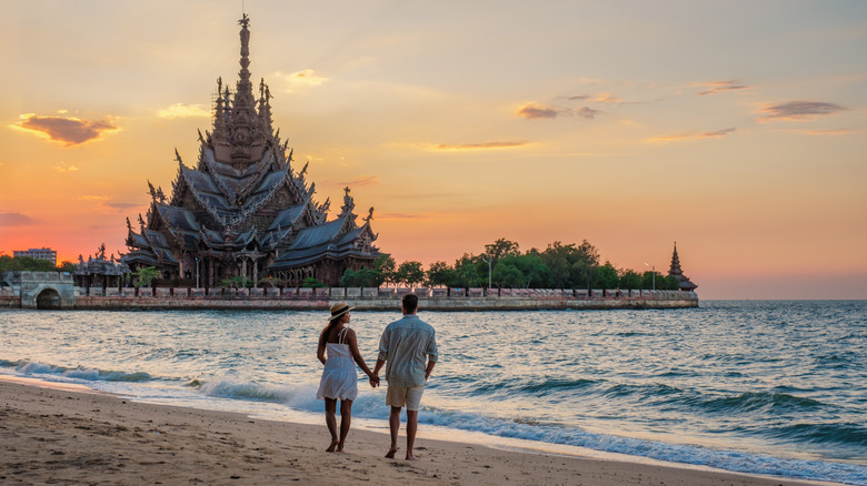 a couple holding hands on a beach with an ornate temple in the background