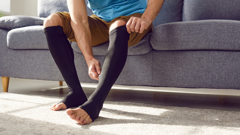 A person putting on black toeless compression socks.