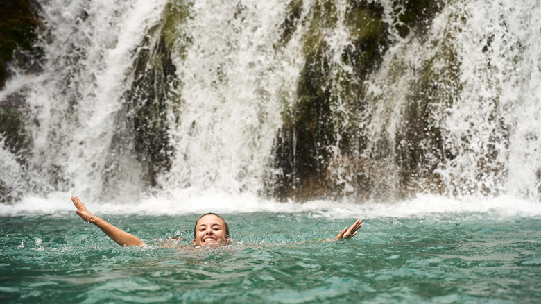 Young traveler swimming near waterfall