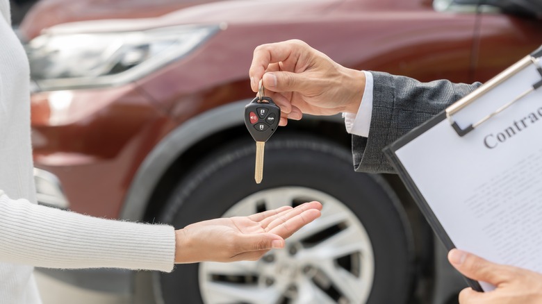 Handing over a car key with vehicle in background