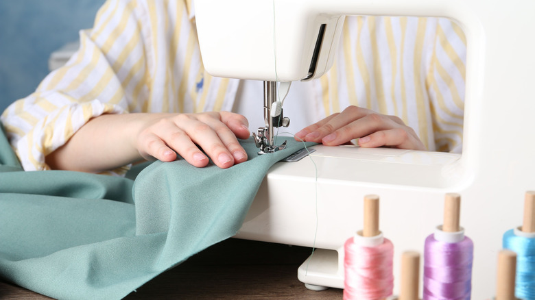 Closeup of hands using a sewing machine with colorful thread in foreground