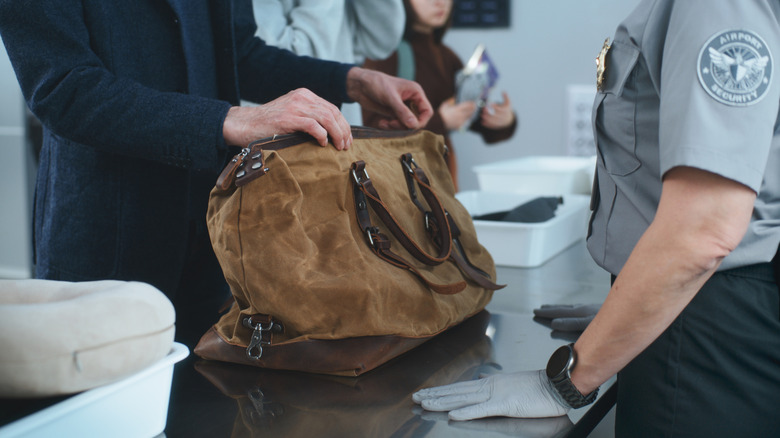 An image showing a person placing a brown carry bag in front of a TSA agent for inspection