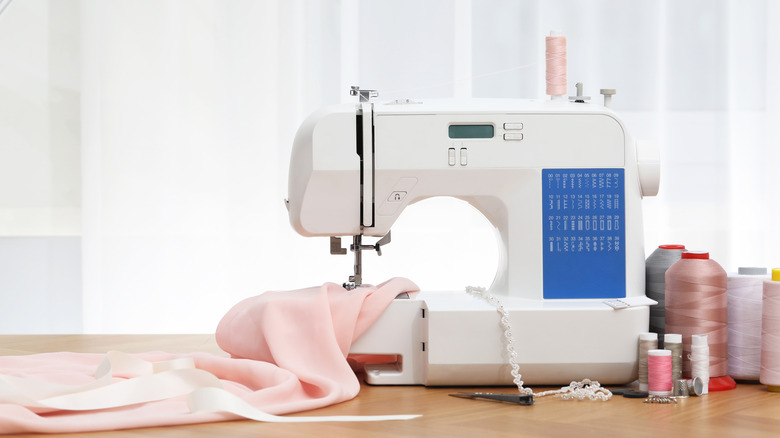 A sewing machine with light pink fabric under the needle with rolls of thread beside it