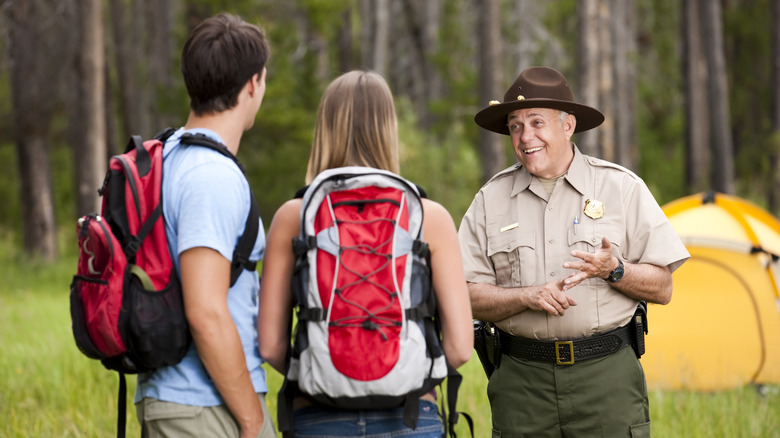 park ranger talking to two backpackers near their tent in the woods