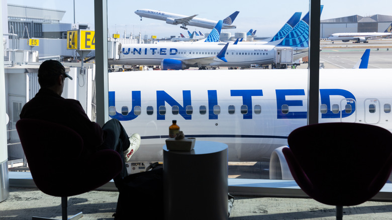 A man sitting in an airport looking out at United Airlines airplanes.