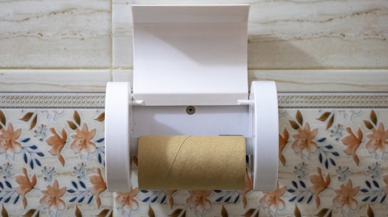 Toilet tissue paper holder with an empty cardboard cylinder on ceramic tile background.