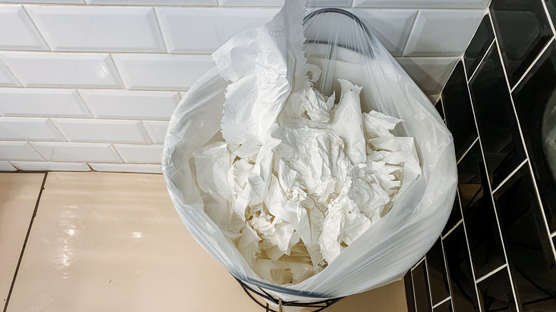 trash can in a tiled bathroom filled with used tissues.