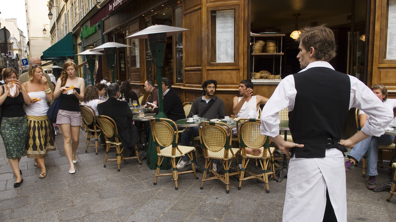 a server with arms akimbo in front of a cafe