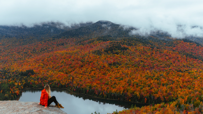 A hiker sitting on a cliff edge looking out over mountains and forest in fall colors
