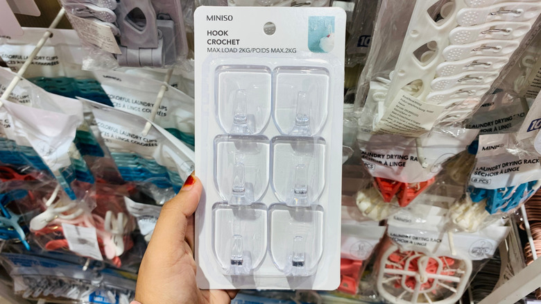 A hand holding a pack of adhesive hooks in a store.