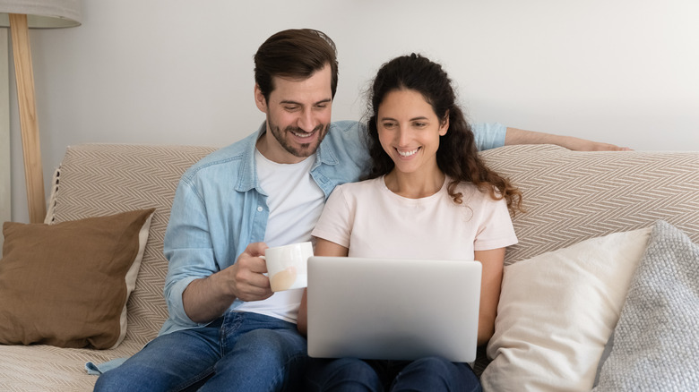 Smiling couple on couch looking at laptop