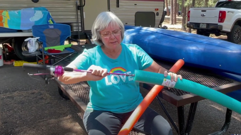 A woman placing a fishing rod inside a pool noodle in front of a camper.