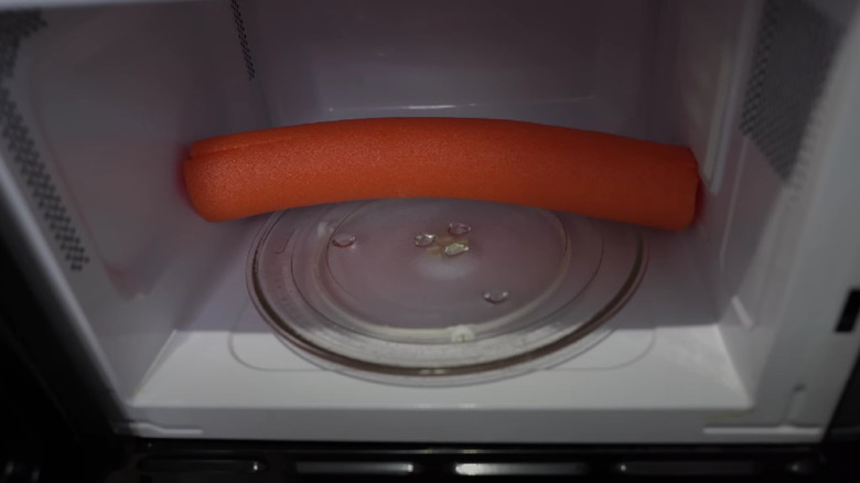 An orange pool noodle wedged in a microwave