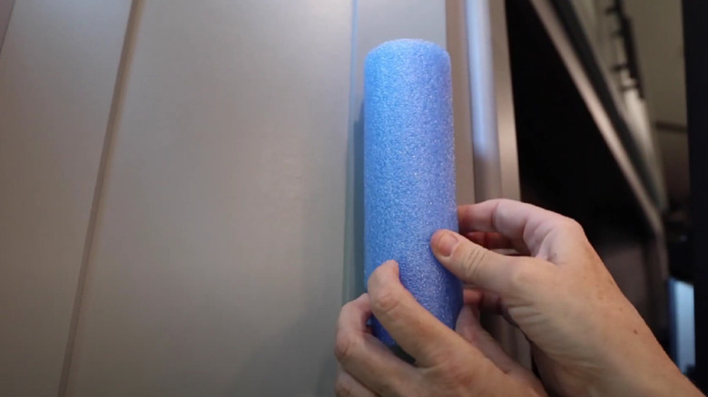 Hands placing a piece of a pool noodle over a cabinet door in an RV.