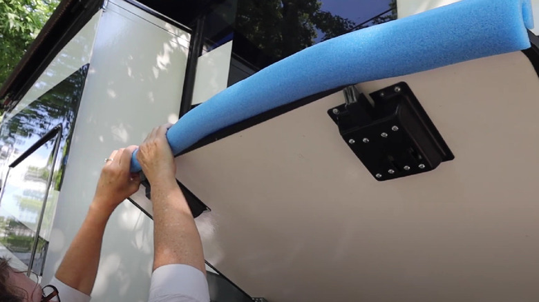 A woman attaches a blue pool noodle to an RV storage door.
